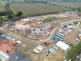 Drone view of new homes being developed in rural Essex, UK. In the distance is arable farmland. Roof beams can be seen on the detached house in the middle of the image.