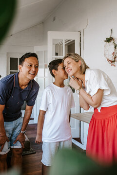 Young boy whispering to her mothers ears while father eavesdrops