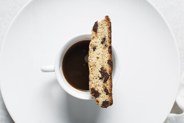 Overhead view of chocolate chip biscotti and coffee on white plate, top view of chocolate chip cantucci cookies on a white plate, flatlay of slices of biscotti cookies or twice baked cookies