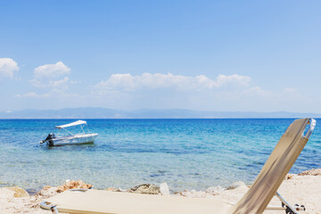 A tranquil Greek beach scene with a boat gently floating in crystal-clear turquoise waters, under a blue sky.  Summer relaxation awaits.