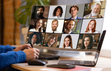 Remote worker in blue sweatshirt taking notes while participating in virtual meeting with...