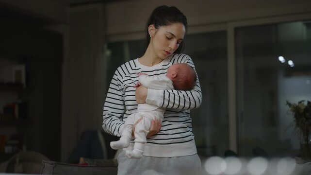Authentic  footage of a mother trying to put her newborn baby to sleep by singing songs and rocking him in her arms. Concept of childhood and parenthood.