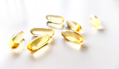 Golden yellow pills in spoon scattered on white background. Softgel capsule of food supplements...