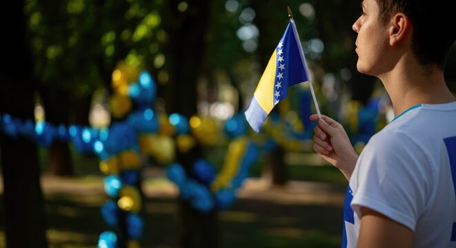 Person holding Bosnia and Herzegovina flag at outdoor event - Powered by Adobe