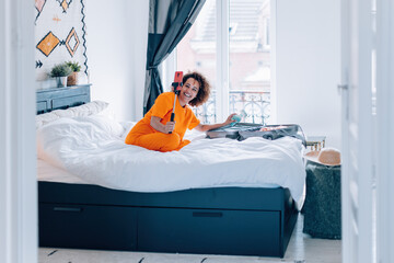 Cheerful woman packing suitcase while recording vlog