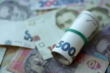 Roll of 500 Ukrainian Hryvnia money bills lies on big pile of ukrainian currency money close up