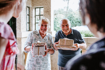 Senior couple bringing gifts greeted at the doorway by grandkids