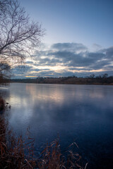 Beautiful blue hour on the lake, trees on the beach , sunrise over the lake with blue sky without clouds.Landscape photography on the pond , purple colors on the sky , trees and water , reflections 
