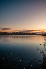 Beautiful blue hour on the lake, trees on the beach , sunrise over the lake with blue sky without clouds.Landscape photography on the pond , purple colors on the sky , trees and water , reflections 