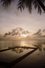 A stunning infinity pool reflecting the golden hues of a tropical sunset over the ocean. A peaceful and luxurious retreat, blending tranquility, elegance, and breathtaking natural beauty in Maldives