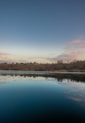 Blue hour on the lake , beautiful landscape photography on the lake with sunrise and reflactions on water , trees on the beach of the lake ,blue and orange colors.Blue sky . Water reflections 