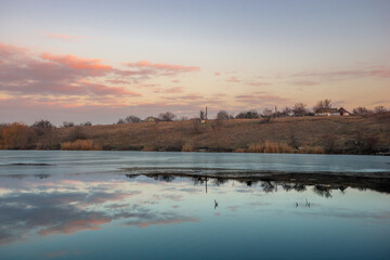 Naklejka premium Blue hour on the lake , beautiful landscape photography on the lake with sunrise and reflactions on water , trees on the beach of the lake ,blue and orange colors.Blue sky . Water reflections 