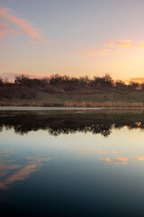 Blue hour on the lake , beautiful landscape photography on the lake with sunrise and reflactions on water , trees on the beach of the lake ,blue and orange colors.Blue sky . Water reflections 