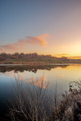 Fototapeta premium Beautiful sunrise on the pond , pond near the village .Red and orange sunrise in the sky , trees and houses , landscape on the lake with sunrise , reflactions on water 