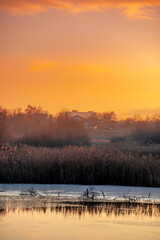 Beautiful sunrise on the pond , pond near the village .Red and orange sunrise in the sky , trees and houses , landscape on the lake with sunrise , reflactions on water 