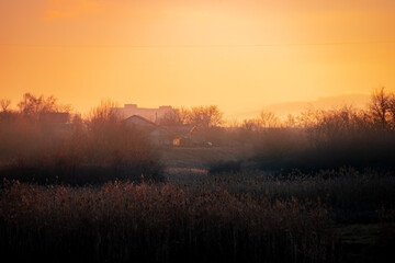 Beautiful sunrise on the pond , pond near the village .Red and orange sunrise in the sky , trees and houses , landscape on the lake with sunrise , reflactions on water 
