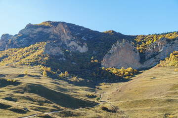 Beautiful landscape featuring rolling hills and towering rock formations under clear blue sky, with...
