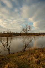 Lake at the october morning , beautiful clouds in the sky , orange colors with blue sky with clouds.Yellow and orange colors.Pond and forest with hills . Trees and water , reflections on lake