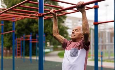 Fototapeta premium Elderly man pulls himself up on a horizontal bar on street sports field