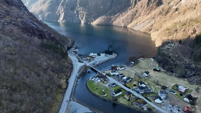 Mowi industrial building with river flowing toward Akrafjorden, surrounded by mountains. Aerial tilt up in winter with no snow
