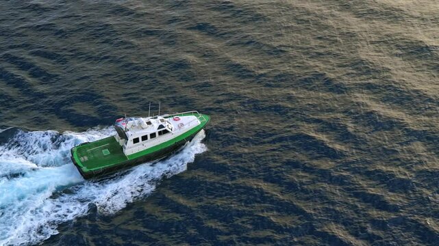 A pilot boat moves at high speed through the waves near Valletta, Malta, leaving a white wake behind. The aerial perspective captures the vessel&rsquo;s motion and the textured water surface in light.