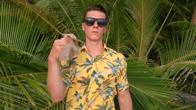 Male tourist fanning himself with Thai Baht bills on tropical beach in Thailand