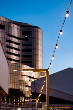 String of lights illuminated in the evening with tall buildings in background
