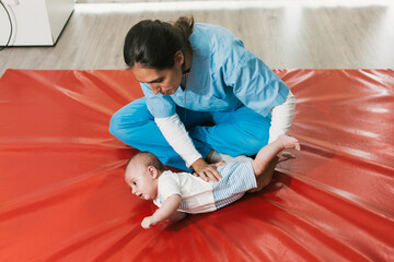 Physiotherapist assisting baby with rolling exercise on red mat