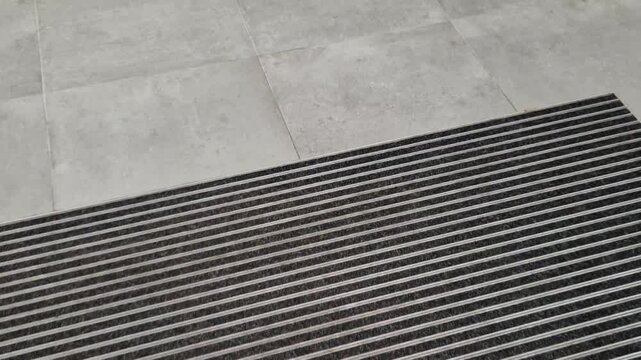 industrial mat cleaning zones at the entrance to the building. A black plastic-metal mat in the shape of an arch or half-circle lies on the limestone mosaic tiles