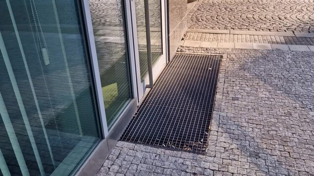industrial mat cleaning zones at the entrance to the building. A black plastic-metal mat in the shape of an arch or half-circle lies on the limestone mosaic tiles