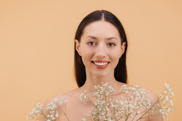 Beautiful smiling woman holding gypsophila flowers is posing in studio on beige background