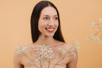 Beautiful smiling woman holding gypsophila flowers looking away on beige background