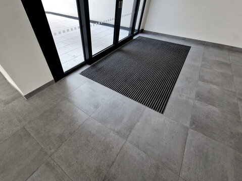 industrial mat cleaning zones at the entrance to the building. A black plastic-metal mat in the shape of an arch or half-circle lies on the limestone mosaic tiles