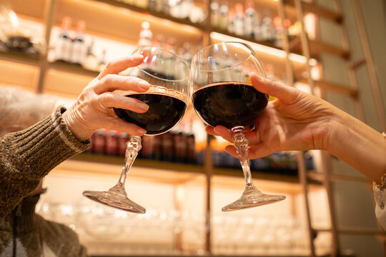 Two women provide with two drinks of red wine from bellow. young and senior. In the background there is an unfocused wines winery. Concept of good life, joy, lifestyle and celebration