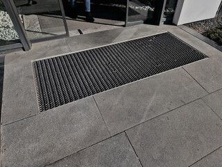 Fototapeta premium industrial mat cleaning zones at the entrance to the building. A black plastic-metal mat in the shape of an arch or half-circle lies on the limestone mosaic tiles