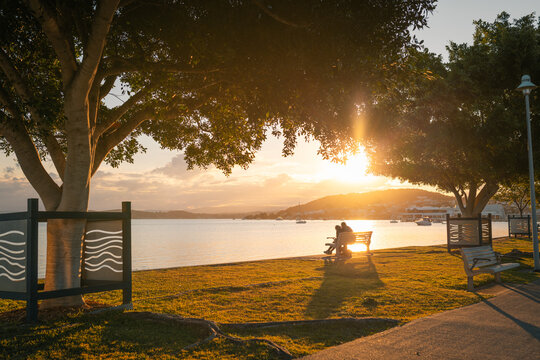 Silhouette of people sitting on park bench beside Lake Macquarie at sunset