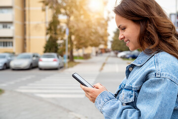 Fototapeta premium Side view of young urban woman using smartphone while standing on a city street