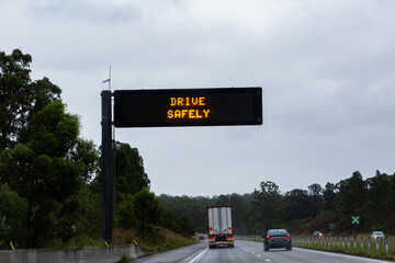 Cars traveling on slippery road with digital sign warning of hazardous driving conditions