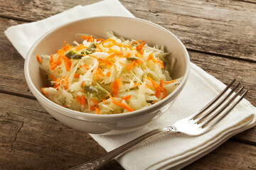 Coleslaw salad with carrots in bowl with napkin and silver fork on rustic table