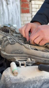 A mechanic's hands working on changing electrical wiring or ignition coils in a car engine.
