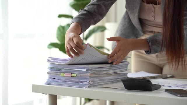 Unveiling the Details: A person meticulously organizes a pile of documents at a work station. revealing a focused professional.