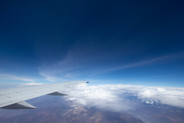 Fototapeta premium Aerial view of cloud blue sky and plane wing view through the airplane window.
