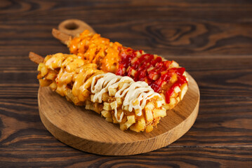 Corn dogs with sausage, cheese, potatoes and sauces on a plate on a wooden table. Korean street food.