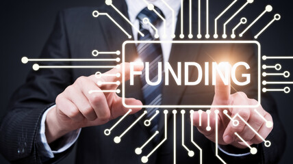 A businessman interacting with a futuristic interface displaying the word "FUNDING," symbolizing digital investment, finance, and technological innovation.