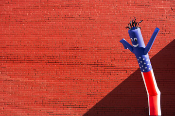 Inflatable tube man with American flag patter against brick wall
