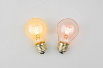 On a white background, a close-up view shows two lightbulbs, one of which is lit while the other is not
