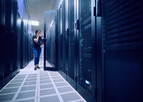 Female technician using laptop and phone in server room&nbsp;