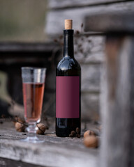 Corked black wine bottle with burgundy label on wooden surface. Glass of rose wine. Wine tasting in fall. Alcohol beverage. Winemaking, winery, vineyard. Outdoor setting. Drink concept. Copy space.