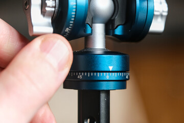 Close-up of a precision-engineered blue anodized metal tripod ball head with adjustment knobs, held...