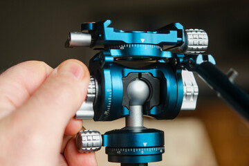 Close-up of a precision-engineered blue anodized metal tripod ball head with adjustment knobs, held...